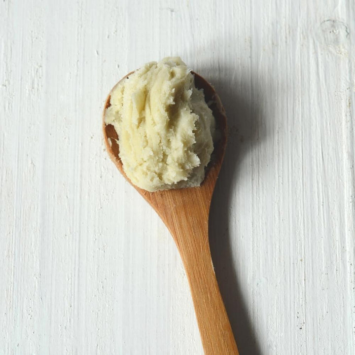 Een lepel shea butter op een wit oppervlak.